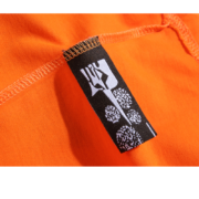 Close-up view of the black brand label on the orange Sp5der Worldwide Star Beluga T-Shirt for authentic identification.