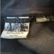 Detailed close-up of the Spyder Outbound Jacket brand tag, logo, and garment information label inside the clothing.