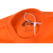 Close-up of an orange Sp5der Arach Tee showing the internal branded neck label with size information and care symbols.