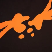 A close-up view of the orange graphic print on a black Sp5der TM Tee showing the brand's iconic design details.