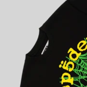 A close-up view of the black Sp5der OG Web V2 t-shirt showing the signature green web and yellow text branding details.