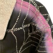 Detailed close-up of the Sp5der trucker jacket featuring a premium rhinestone spider web graphic and shearling collar.