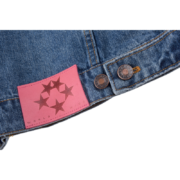 Close-up of the pink branded logo patch and metallic button on the SP5DER Worldwide denim jacket for streetwear