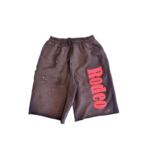 Front view of the Sp5der x Cactus Jack Rodeo shorts featuring pink lettering and star accents on dark fabric.