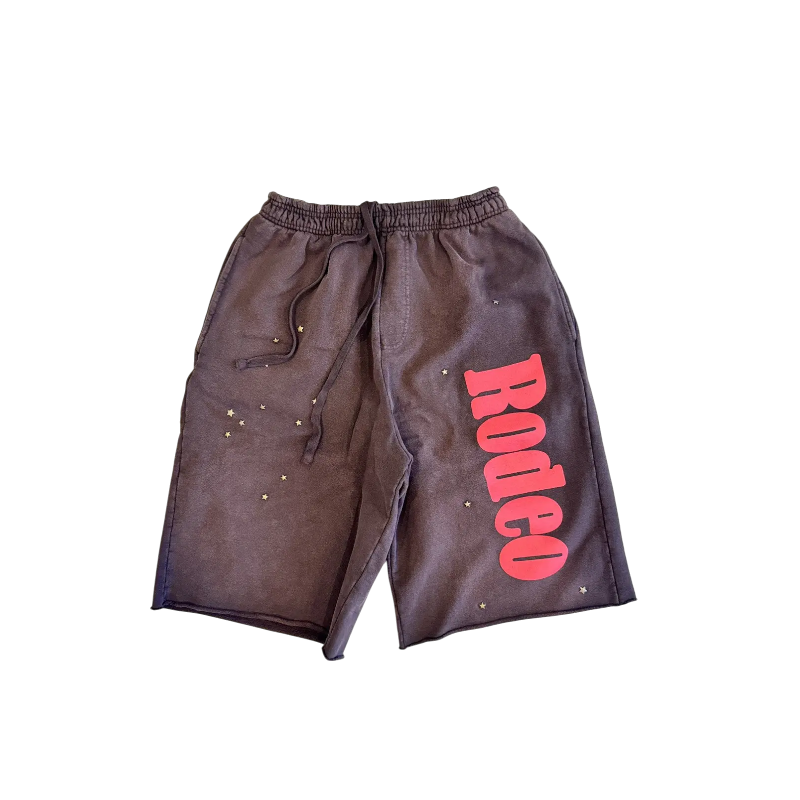 Front view of the Sp5der x Cactus Jack Rodeo shorts featuring pink lettering and star accents on dark fabric.