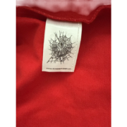 Close-up view of the official white Sp5der neck tag featuring a black web logo on a red fabric Sp5der denim jacket.
