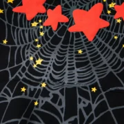 Close-up of the black Sp5der Atlanta Star-Print hoodie fabric featuring a prominent spiderweb and red star pattern.