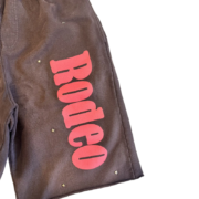 Detailed view of the Sp5der x Cactus Jack Rodeo short, featuring premium dark fabric with bold pink rodeo lettering.