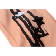 Close-up view of the Sp5der Bellini sweatpants featuring a vibrant peach fabric and premium black distressed print detail.