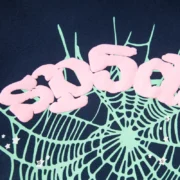 Close-up of the Sp5der OG Web Hoodie in navy blue featuring a bold, light green spider web graphic and pink logo text.