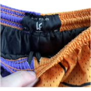 Close-up of the Lost Files interior brand label and waistband on the purple and orange split Sp5der web mesh shorts.