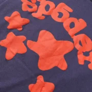 Close up detail of the navy-blue Sp5der Beluga hoodie featuring premium fabric and bright orange star graphic prints.