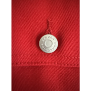 Close-up of a silver Sp5der Worldwide branded metal button on a premium bright red denim jacket fabric detail.