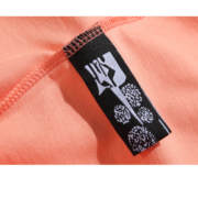 Close-up view of a peach-colored Sp5der Print t-shirt featuring the signature black brand neck label with white logo.