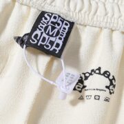 Close up of the brand label tag on the cream Sp5der x Mariah the Scientist Scorpion sweatpants, size medium.