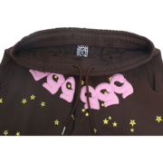 A close-up view of the brown Sp5der 555 555 sweatpants featuring the signature pink lettering and yellow star pattern.