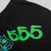 Close-up view of the black SP5DER x 999 Club 555 sweatpants featuring signature green graphic print design details.