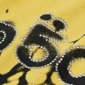 Close-up of Sp5der Scattered OG Web V2 yellow tee featuring a black spiderweb print and rhinestone-studded lettering.