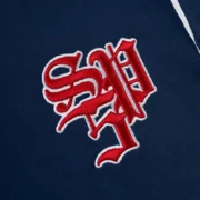 Close-up view of the detailed red Sp5der Academy logo embroidered on the navy cotton fabric of the rugby shirt.