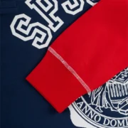 Close-up view of the Sp5der Academy Rugby Navy graphic featuring white letter print and bold red sleeve details.