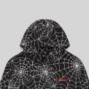 Close-up of the black Sp5der hoodie featuring an all-over white embroidered web design and a signature chest logo.