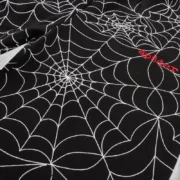 Close-up view of black Sp5der sweatpants featuring an embroidered white all-over web design and a signature red logo.
