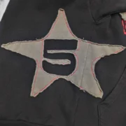 Detailed close-up of the frayed star patch graphic on the black Sp5der Big Star full zip hoodie streetwear jacket.