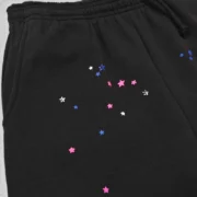 Close-up view of the black Sp5der CB Punk V2 sweatpants featuring a scattered multi-colored star graphic print design.