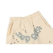 Close-up view of the branding and star graphic details on the cream-colored Sp5der Cropped Sweatpants streetwear.