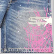Close-up view of the Sp5der Heavy Web Denim Shorts in light blue featuring a detailed pink graphic web design print.