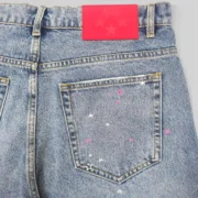 Close up view of the back pocket on Sp5der Heavy Web light blue denim shorts featuring a bright red leather waist label.