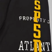 Close-up of Sp5der Issue 404 black sweatpants showing raised yellow chenille lettering and faded white graphic print.