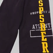 Close-up view of the black Sp5der Issue 404 sweatpants featuring signature yellow chenille SPSDER lettering details.