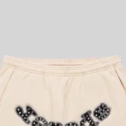 Close-up of Sp5der Mixed Stone OG Logo sweatpants in cream, featuring studded and embellished appliqué detailing.