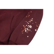 Close-up view of the sleeve on the maroon Sp5der Nocturnal Highway Hoodie featuring unique paint splatter detailing.
