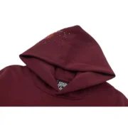 Detailed close-up view of the Sp5der Nocturnal Highway Hoodie in maroon, focusing on the hoodie hood and brand logo.