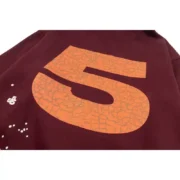 Close up view of the maroon Sp5der Nocturnal Highway hoodie showing the large textured orange logo detail on the chest