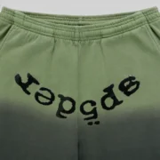 Close-up view of Sp5der OG Web Ombre Sweatpants in black featuring a unique black puff print logo on green fabric.