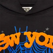 Close-up view of the Sp5der OG Web V2 Knicks Alternate Hoodie in black featuring front orange and blue graphic print.
