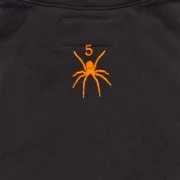 Close-up view showing the iconic orange Sp5der logo graphic print on the back of the black OG Web V2 Knicks hoodie.