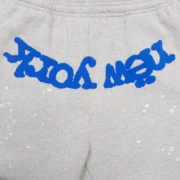 Closeup view of the grey Sp5der OG Web V2 Knicks Home sweatpants featuring signature blue graphic branding details.