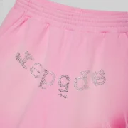 Close-up of Sp5der OG Web V2 Spray Zip Sweatshorts in Light Pink featuring rhinestone SP5DER logo detail.