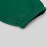 Close-up view of the green cotton fleece fabric and elastic hem cuff on the Sp5der OG Web Studded Sweatpants.