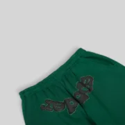 Close up view of the green Sp5der OG Web Studded Sweatpants featuring signature web print and heavy duty hardware studs.