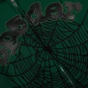 Close-up view of the green Sp5der OG Web Studded Zip Hoodie featuring black spider web graphics and stud detailing.