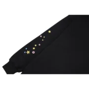 Close-up view of the black Sp5der P*NK hoodie sleeve featuring detailed colorful star and branding graphic prints.