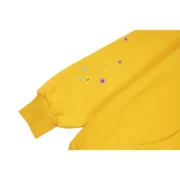 Close-up view of the sleeve detail on the Sp5der P*NK Hoodie in a vibrant mustard-yellow colorway with graphic prints.
