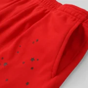 Close-up of red Sp5der P*NK V2 fleece sweatpants featuring premium 23oz fabric and signature black star print detail.