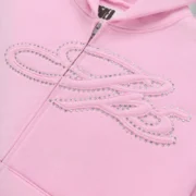 Close-up view of the Sp5der Rhinestone Script Zip Hoodie in Light Pink featuring sparkling rhinestone logo detail.