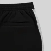 Close-up view of the black Sp5der Screaming Eagle sweatpants featuring a unique white sprayed-effect side stripe detail.